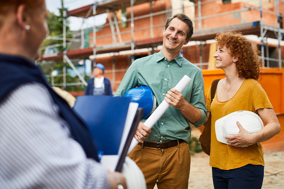 Zwei Personen auf einer Baustelle mit einem Haus im Hintergrund