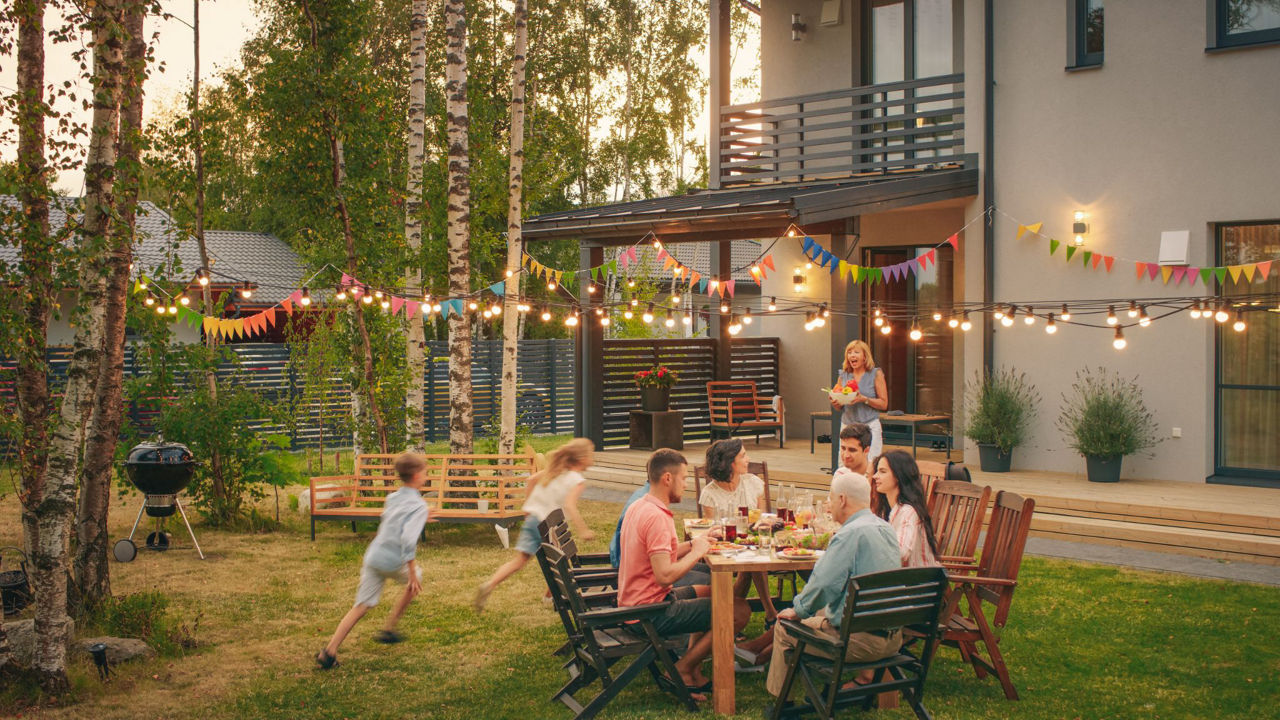 Famile mit Gästen im Garten am Tisch, Kinder rennen