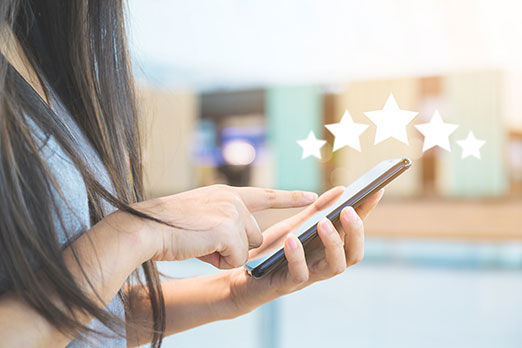 Eine Frau tippt auf ihr Smartphone, über dem digitale Sterne als Bewertungssymbol erscheinen.