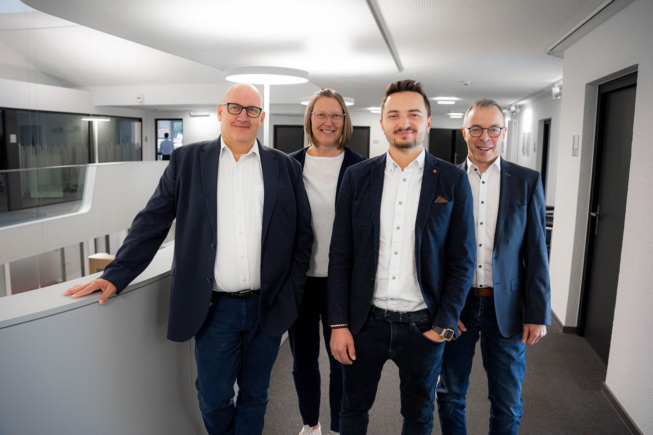 Vier Personen in Geschäftskleidung stehen gemeinsam in einem modernen Büroflur.