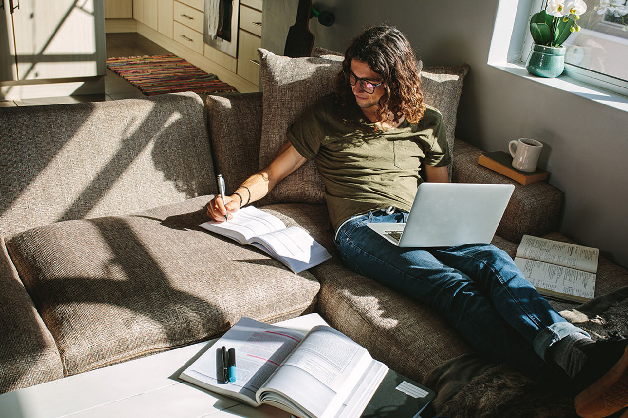 Frau auf dem Sofa mit Laptop und Büchern 
