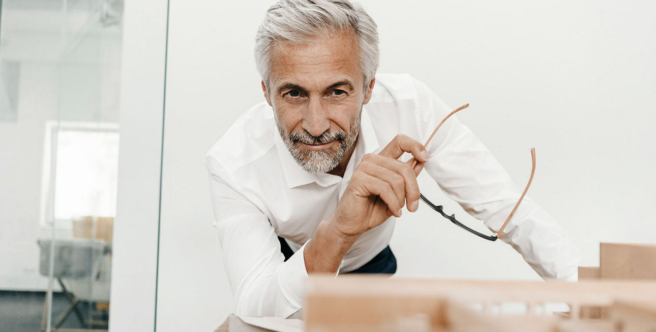 Mann mit Brille in der Hand schaut auf das Modell einer Immobilie