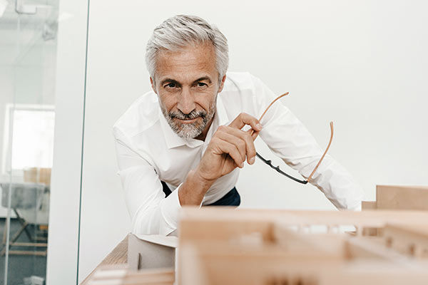 Mann mit Brille in der Hand schaut auf das Modell einer Immobilie