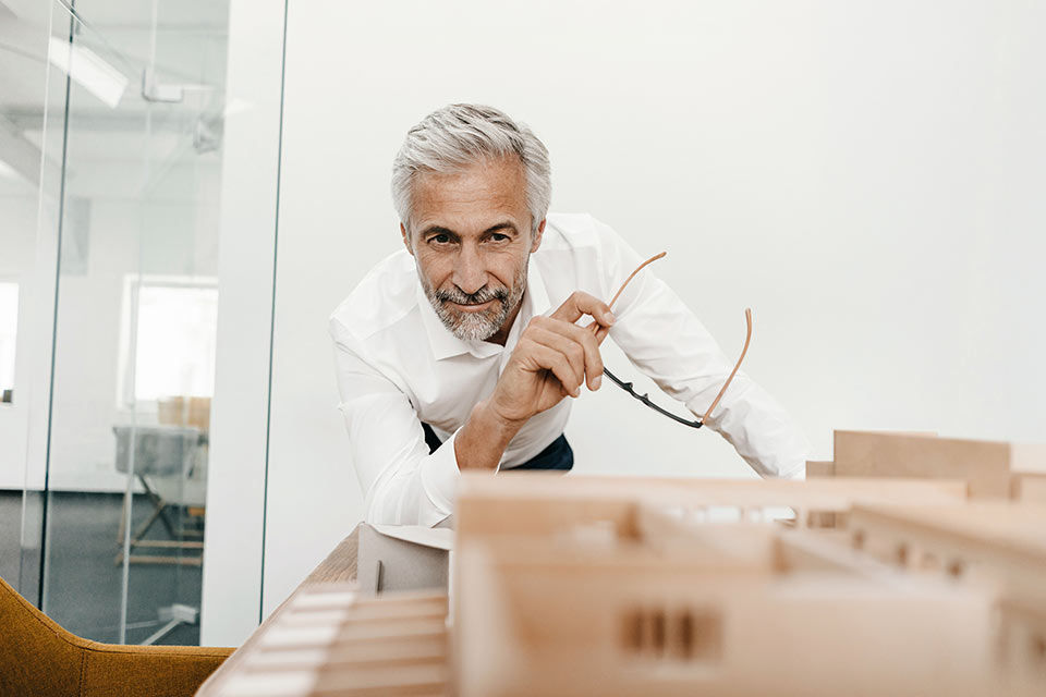 Mann schaut auf ein Immobilienmodell mit Brille in der Hand