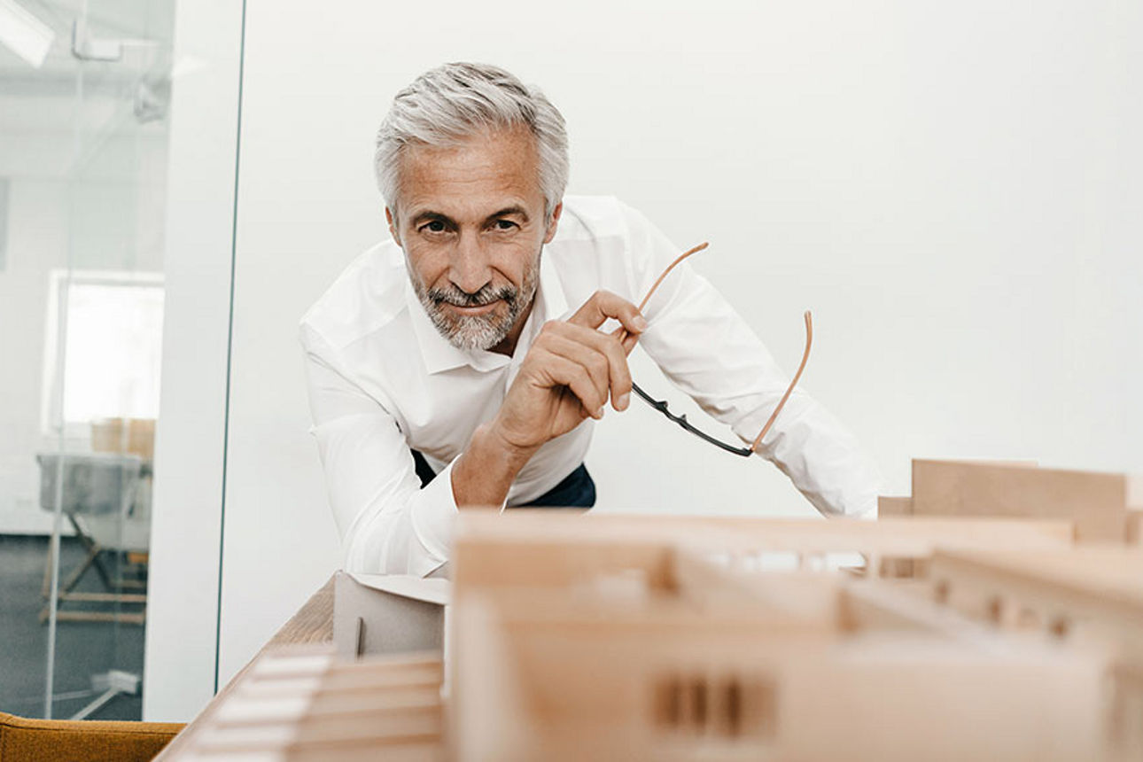 Mann schaut auf ein Immobilienmodell mit Brille in der Hand