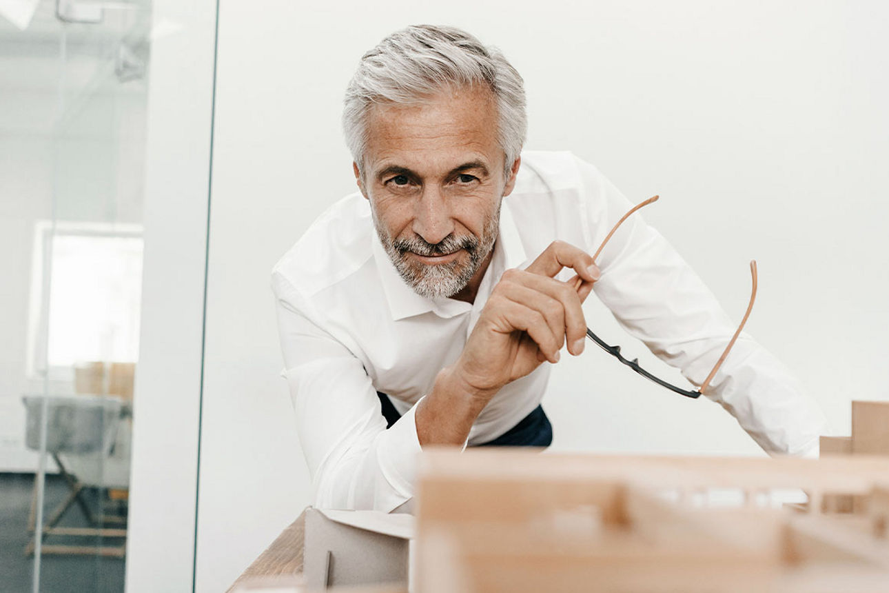 Mann mit Brille in der Hand schaut auf das Modell einer Immobilie