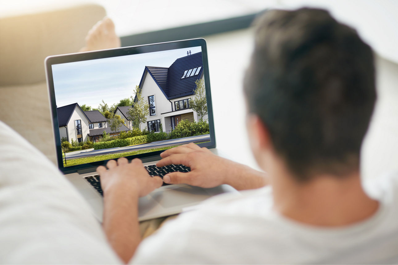 Mann sitzt auf dem Sofa am Laptop und schaut nach Immobilien