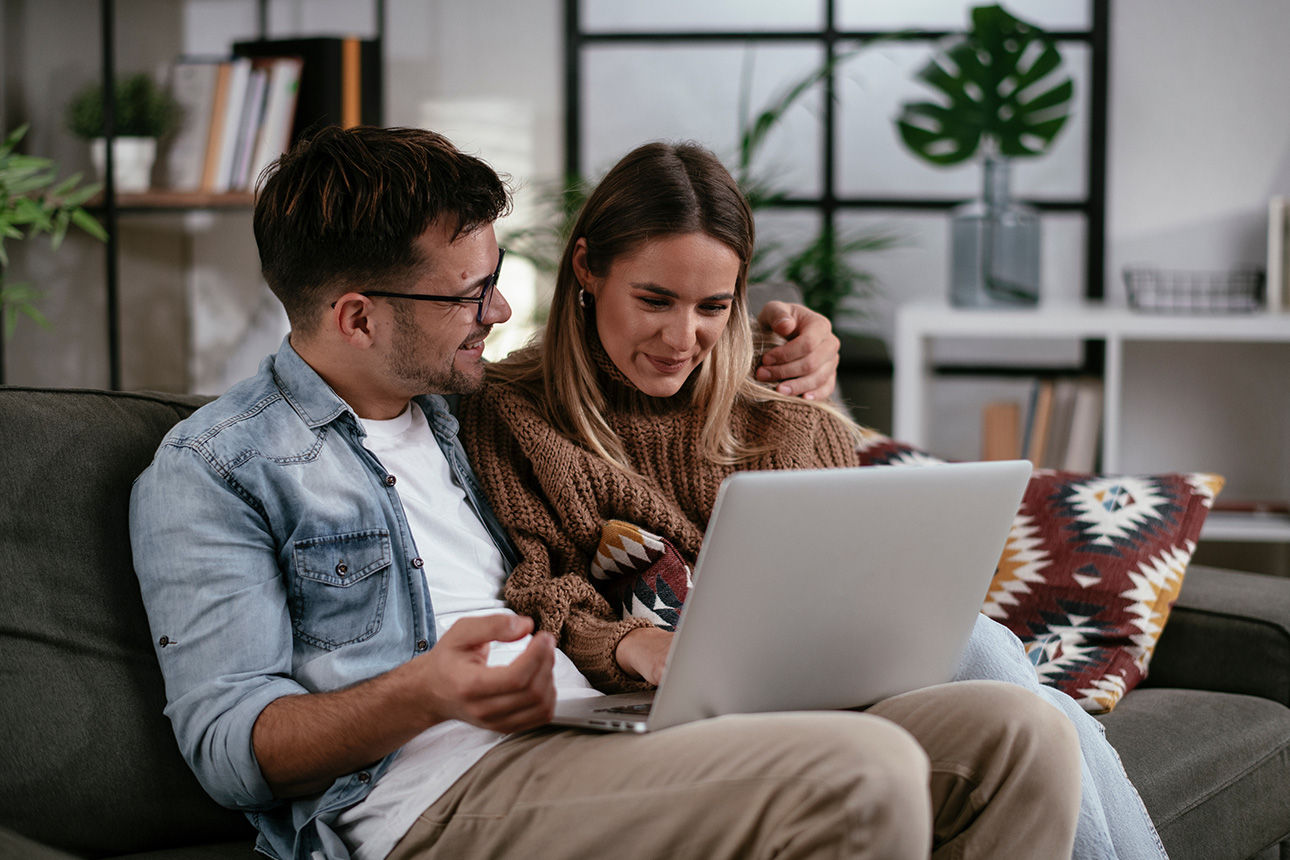 Pärchen sitzt auf dem Sofa und schaut auf einen Laptop