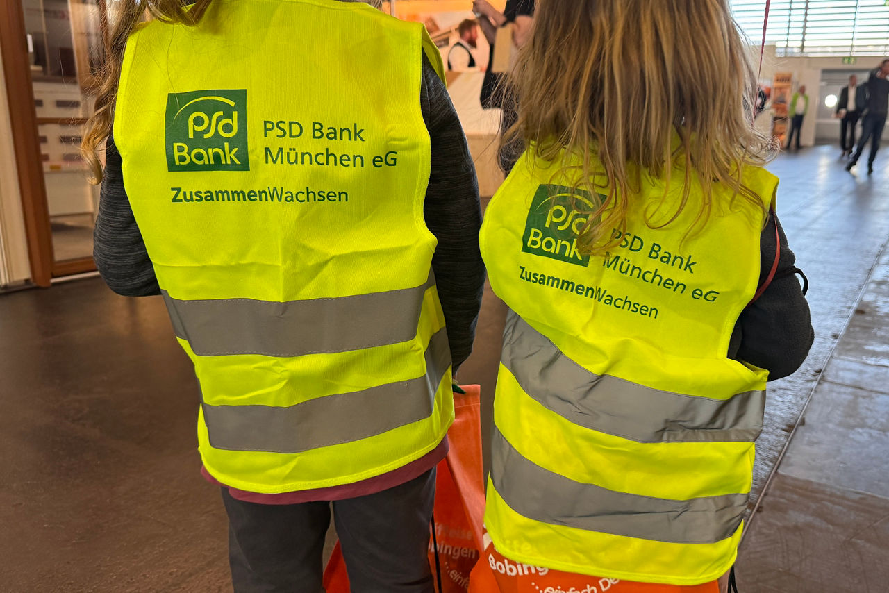Zwei Mädchen von hinten. Beide tragen die PSD Bank München Kinder-Warnweste.