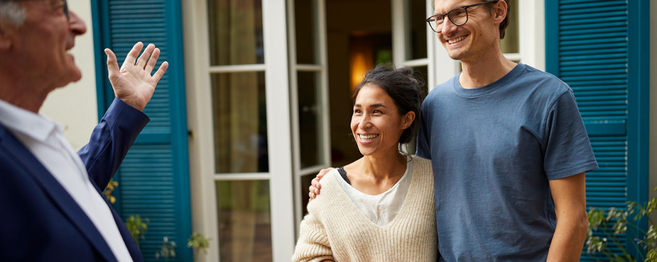 Immobilienmakler mit jungem Paar vor einer Immobilie