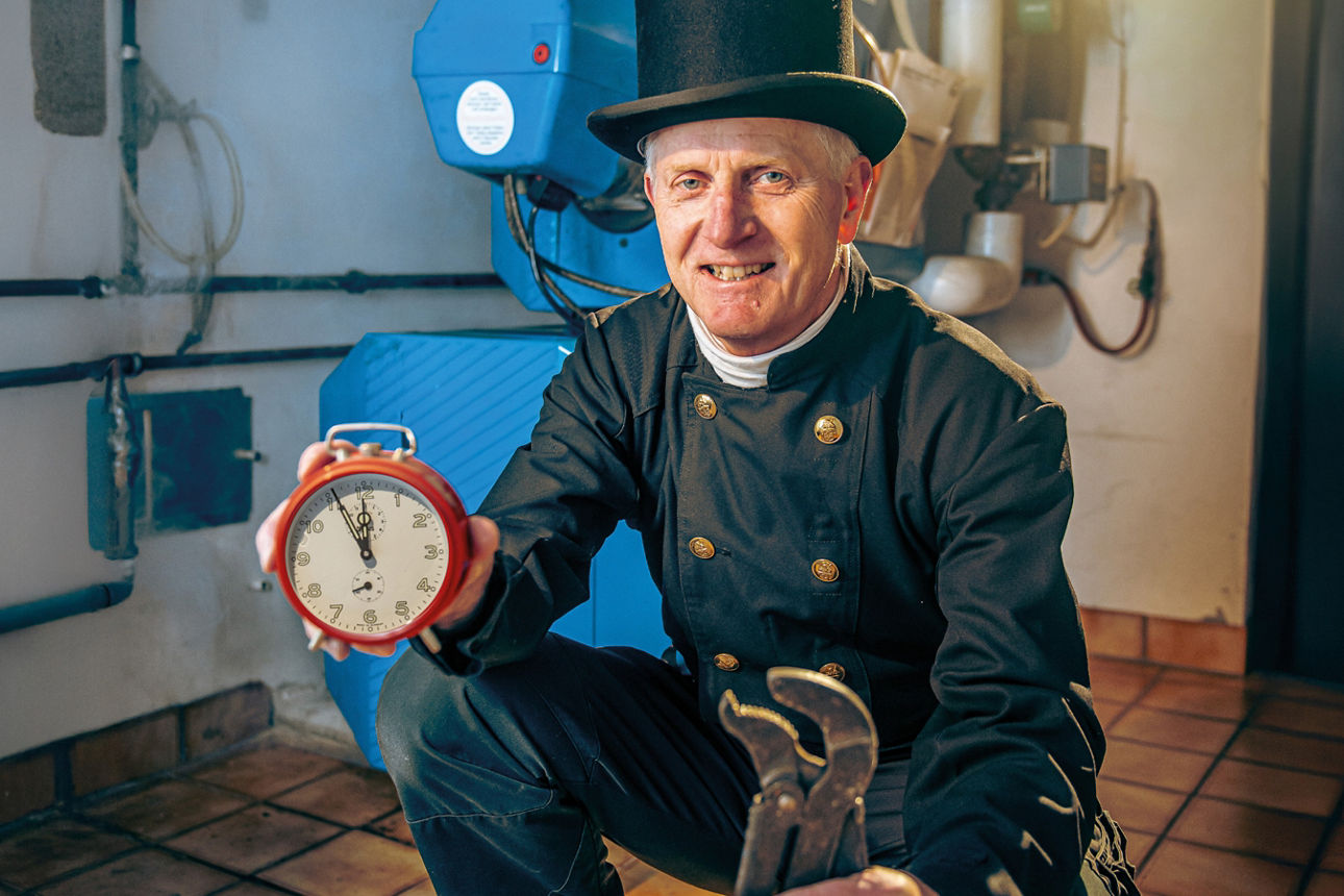 Schornsteinfeger mit Wecker und Werkzeug in der Hand