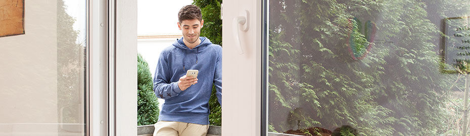 Ein junger Mann steht in einem Hauseingang und schaut auf sein Handy