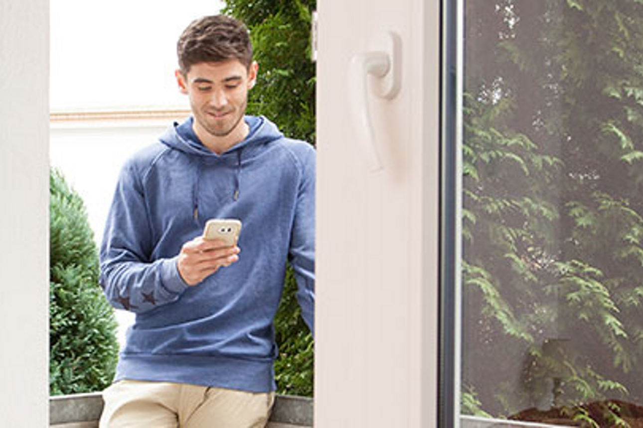 Ein junger Mann steht in einem Hauseingang und schaut auf sein Handy