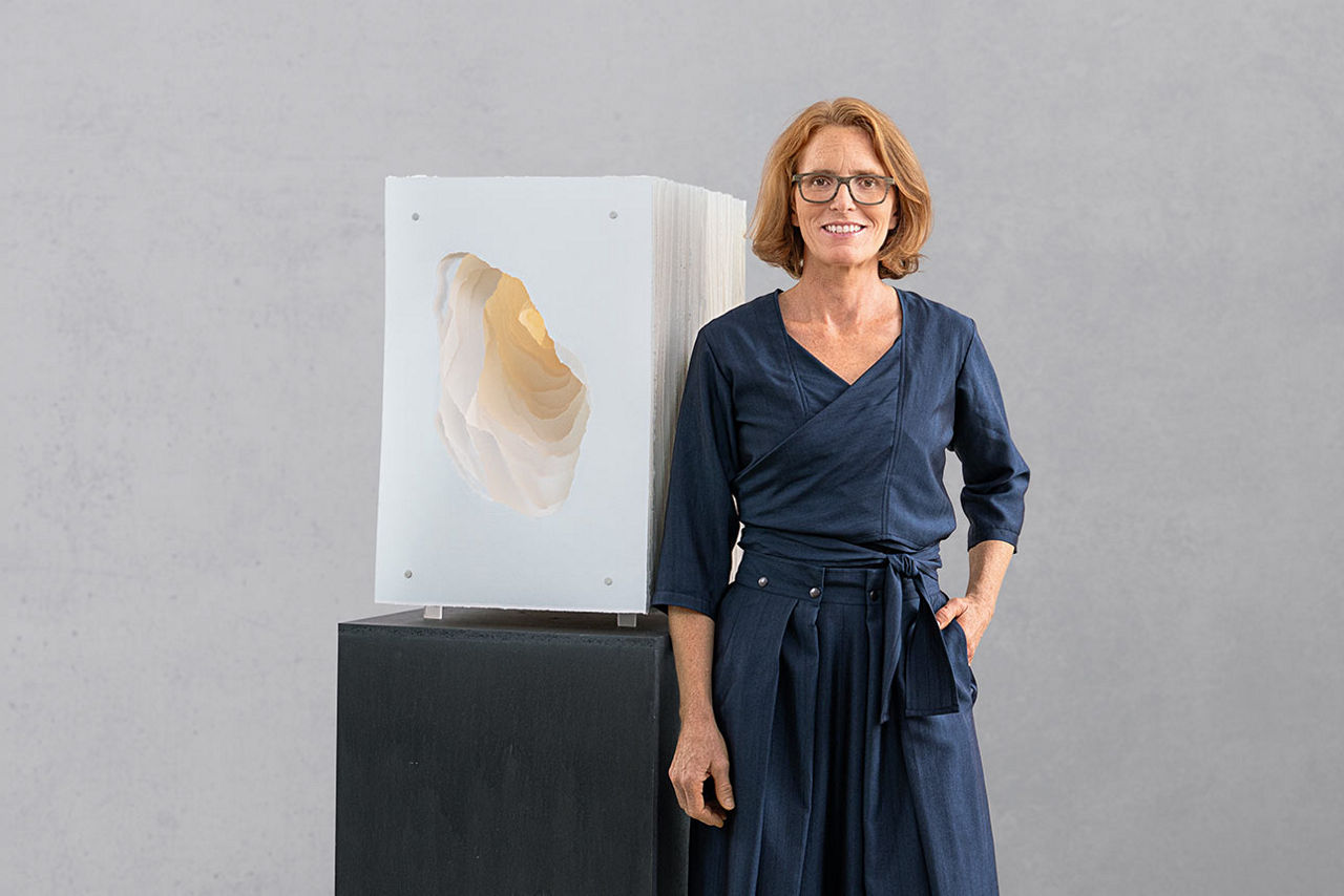 Die Künstlerin Angela Glajcar steht vor einem Ihrer Werke, einer Skulptur auf schwarzem Sockel
