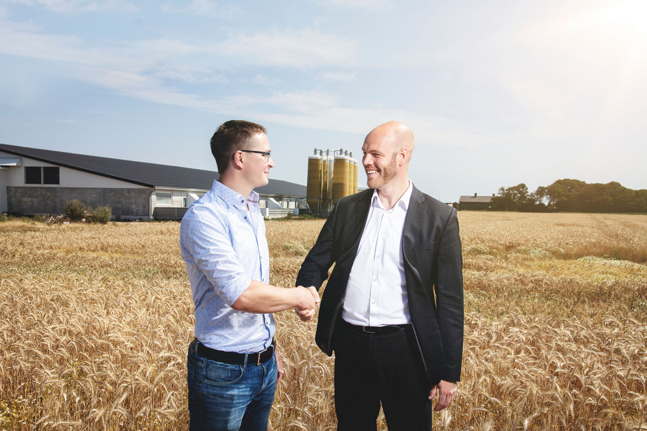 Zwei Männer stehen auf einem Getreidefeld und geben sich die Hand