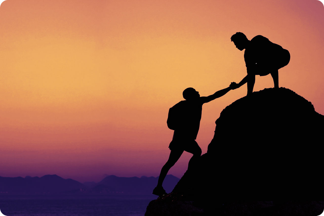 Ein Bergsteiger hilft einem anderen Bergsteiger auf den Gipfel