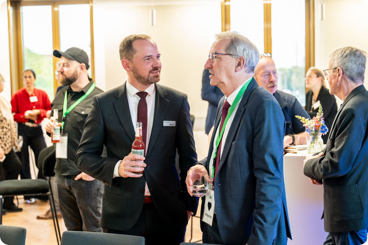 Teilnehmende eines Netzwerktreffens stehen bei Gesprächen in einem Veranstaltungsraum zusammen.