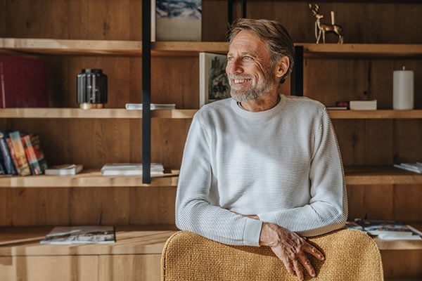Ein lächelnder Mann mit grauem Bart steht vor einem Holzregal
