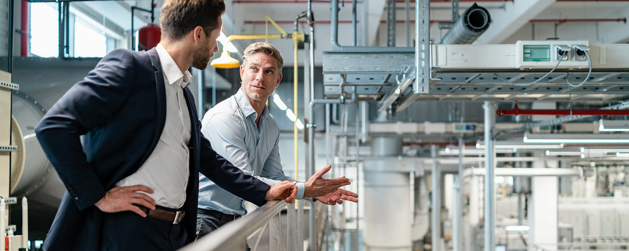 Zwei Männer stehen an einem Geländer innerhalb einer Produktionsanlage