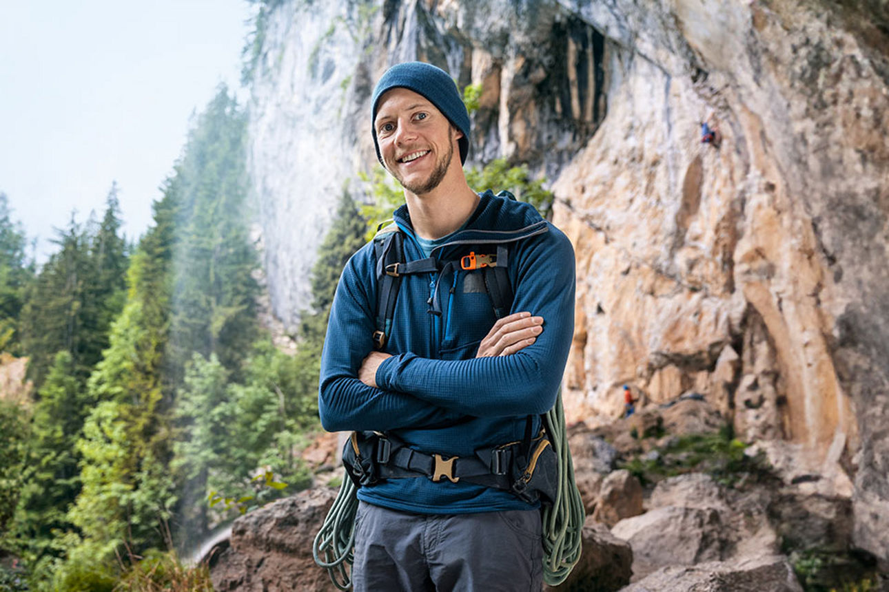 Mann steht mit verschränkten Armen vor einem Felsen