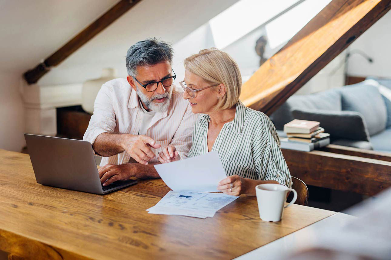 Paar sitzt mit Dokumenten gemeinsam vor einem Laptop