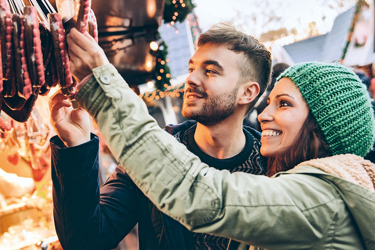 Ein Pärchen auf einem Adventsmarkt, die sich gerade Süßwaren genauer anschauen