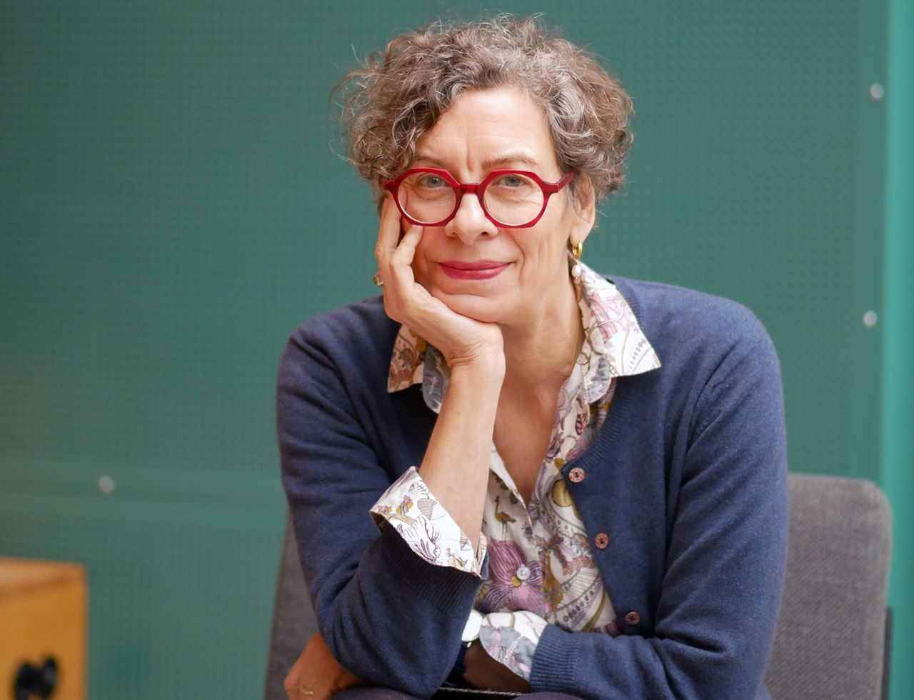 Frau Dr. Jeanette Hofmann sitzt auf einem Stuhl, mit Brille und kurzen Haaren vor grünem Hintergrund