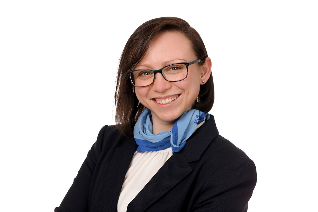 Jennifer Einolf, trägt Brille, einen Bob und ein blaues Halstuch auf weißem Oberteil mit schwarzem Blazer