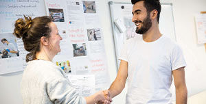 zwei Menschen geben sich die Hand, beide lächeln