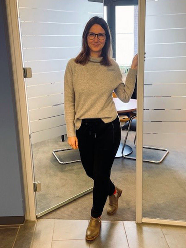 Mitarbeitende mit Brille steht lässig mit einer Hand an einer Bürotür 