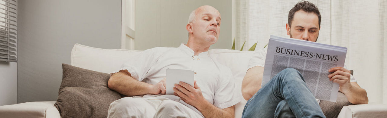 Eine Person liest eine Zeitung und eine zweite sieht mit rein