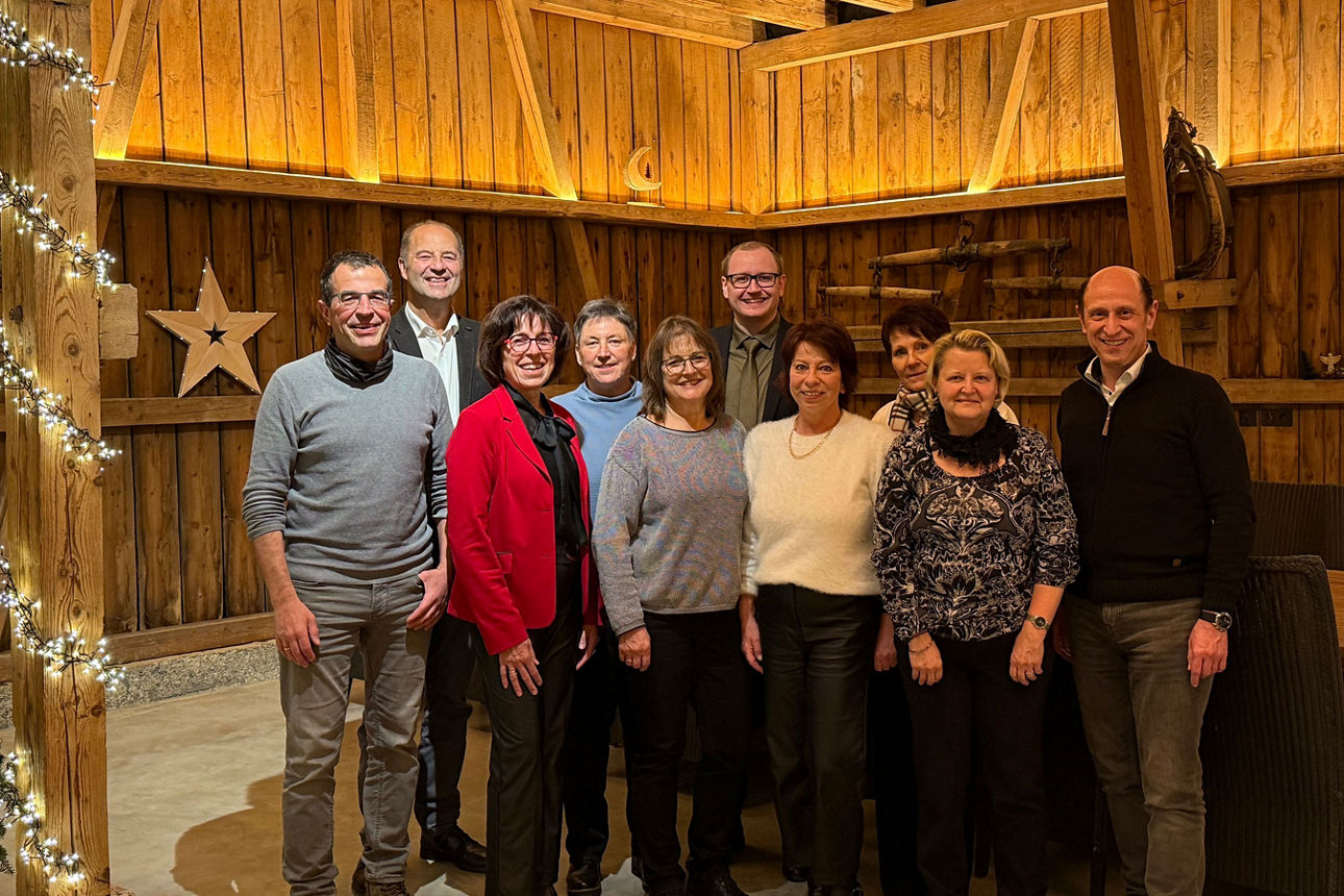 Gruppe von Erwachsenen steht lächelnd in einer festlich geschmückten, gemütlichen Holzscheune zusammen.