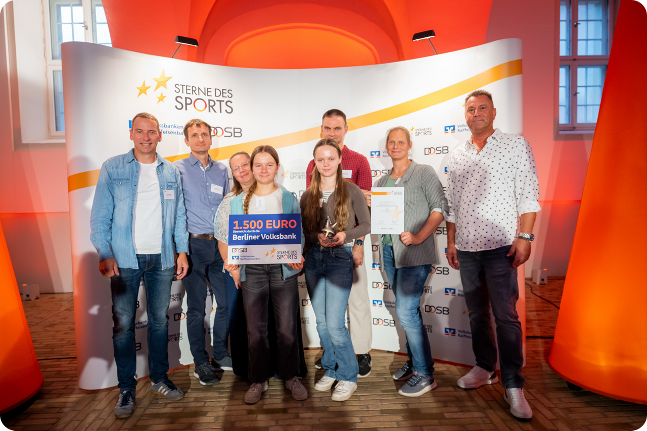 Ein Mädchen hält einen Gewinnscheck über 1500 Euro hoch und ein anderes Mädchen den Stern des Sports in Bronze