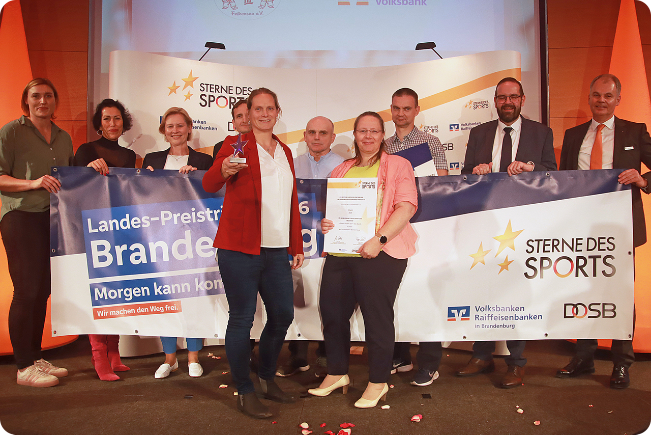Zwei Frauen stehen vor einer Gruppe auf der Bühne und halten Preise hoch