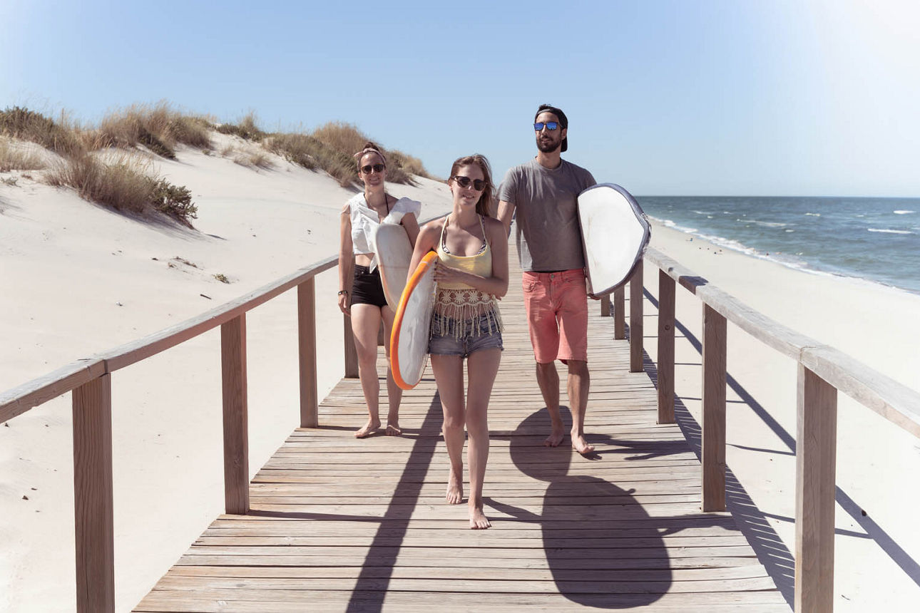 Boys and girls teen surfers with surfboards walking on a wooden pathway at the beach.