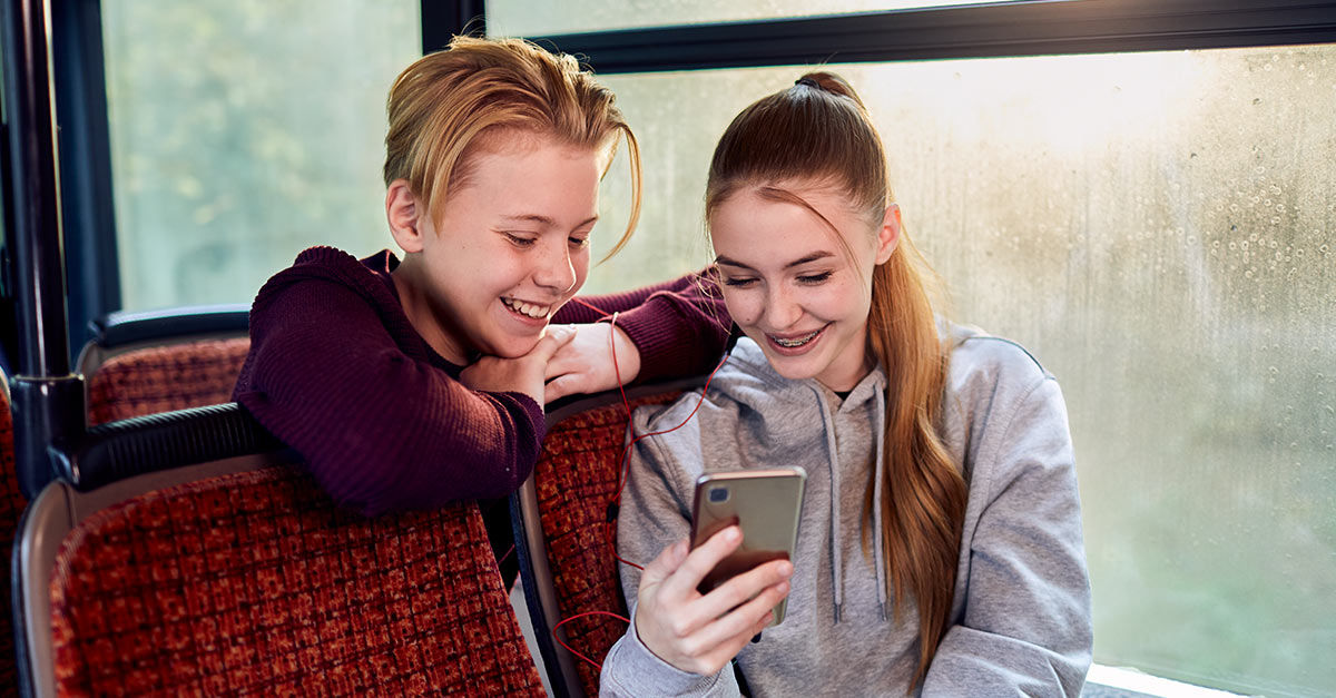 Zwei Kinder schauen im Bus aufs Smartphone