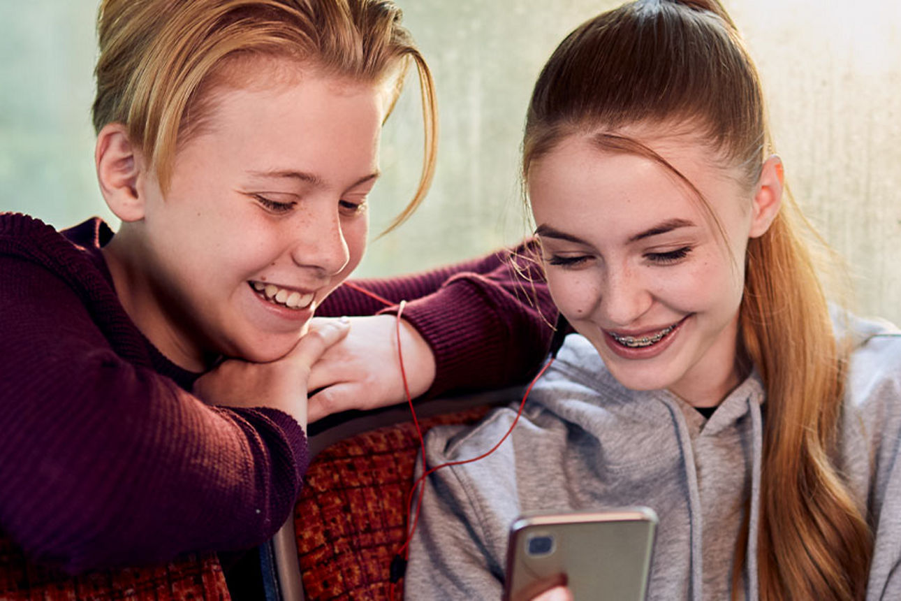 Zwei Jugendliche im Bus schauen auf ein Smartphone