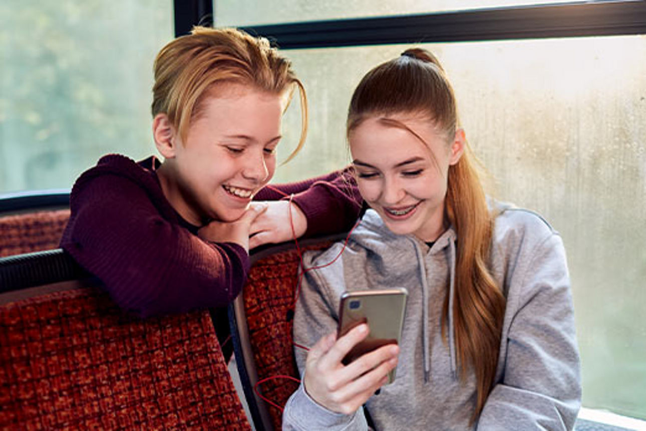 Zwei Jugendliche im Bus schauen auf ein Smartphone