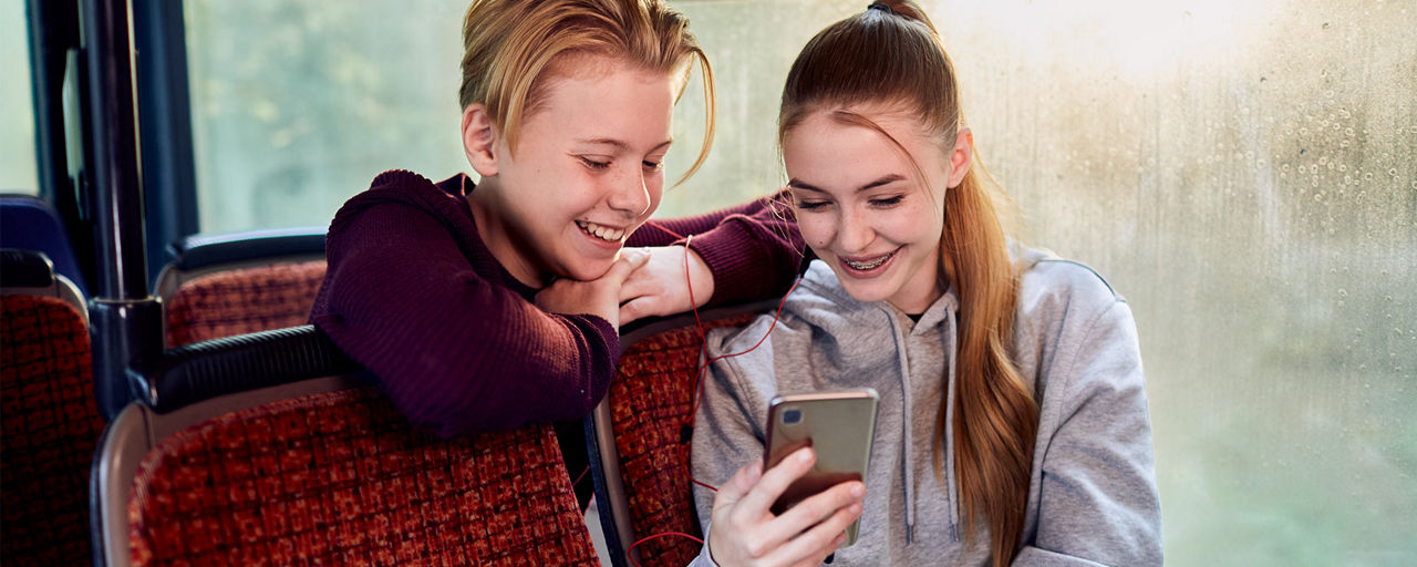 Zwei Jugendliche im Bus schauen auf ein Smartphone