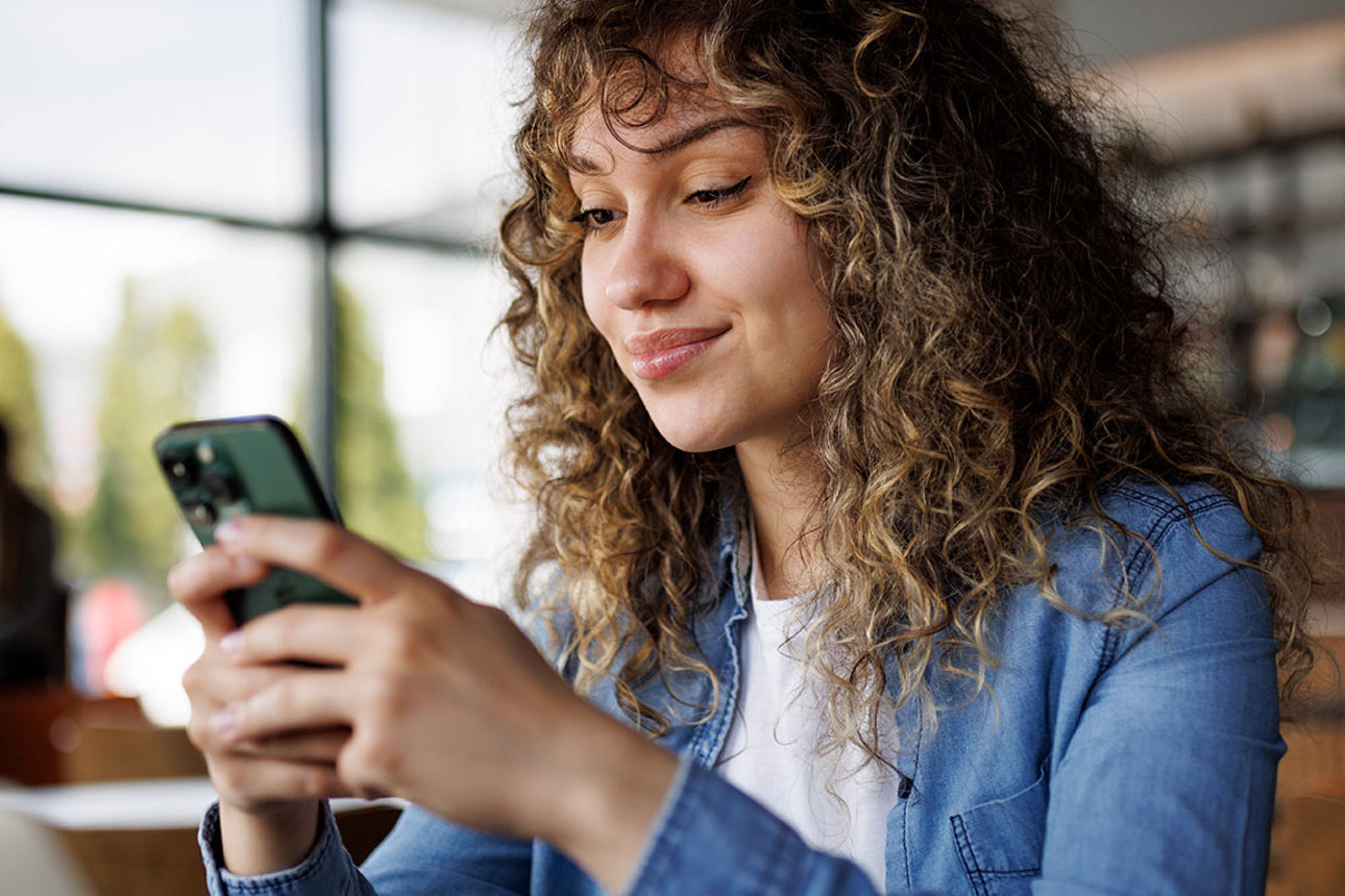 Junge Frau blickt lächelnd in ihr Smartphone