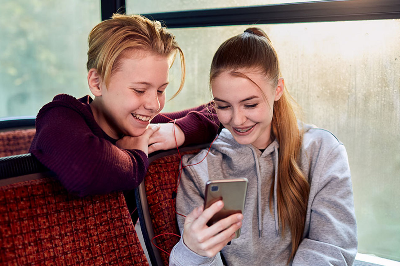 Zwei Kinder schauen im Bus aufs Smartphone