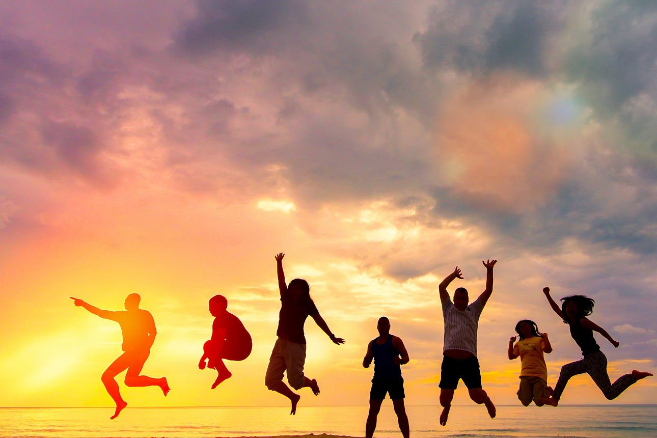 Gruppe junger Menschen springt gemeinsam in die Luft vor einem Sonnenuntergang am Meer