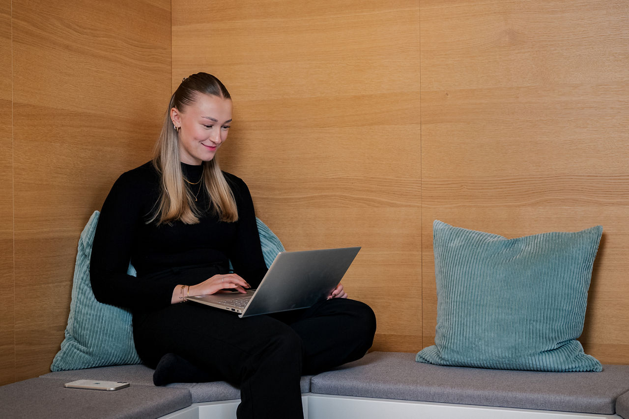 Eine junge Frau sitzt am Laptop in einer Sitzecke