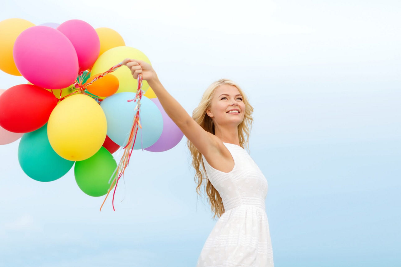 Junge Frau im weißen Kleid mit bunten Luftballons