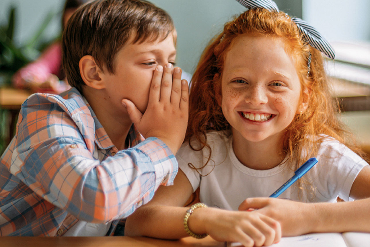 Zwei Kinder nebeneinander auf der Schulbank.