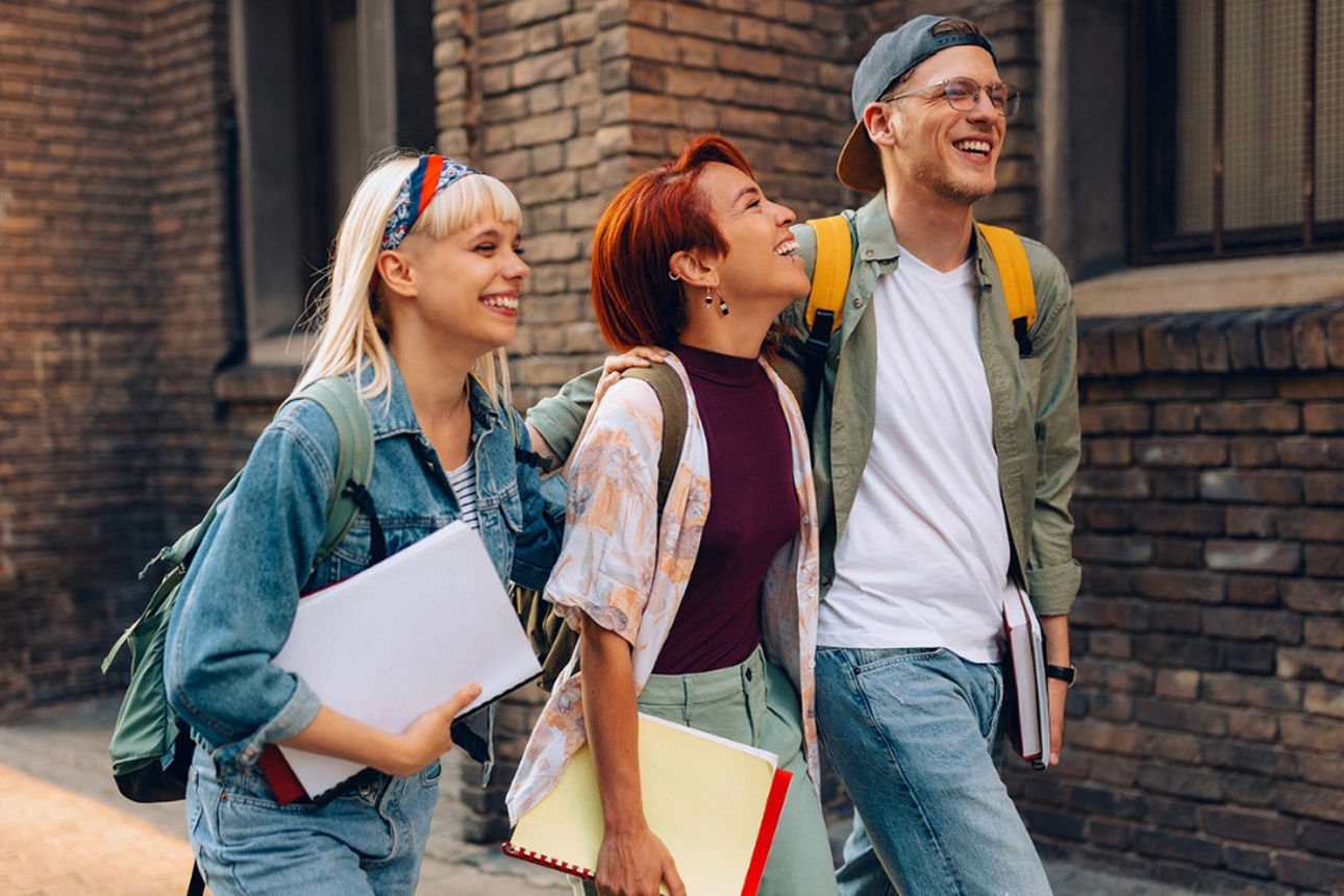 Drei junge Erwachsene gehen gut gelaunt nebeneinander her.