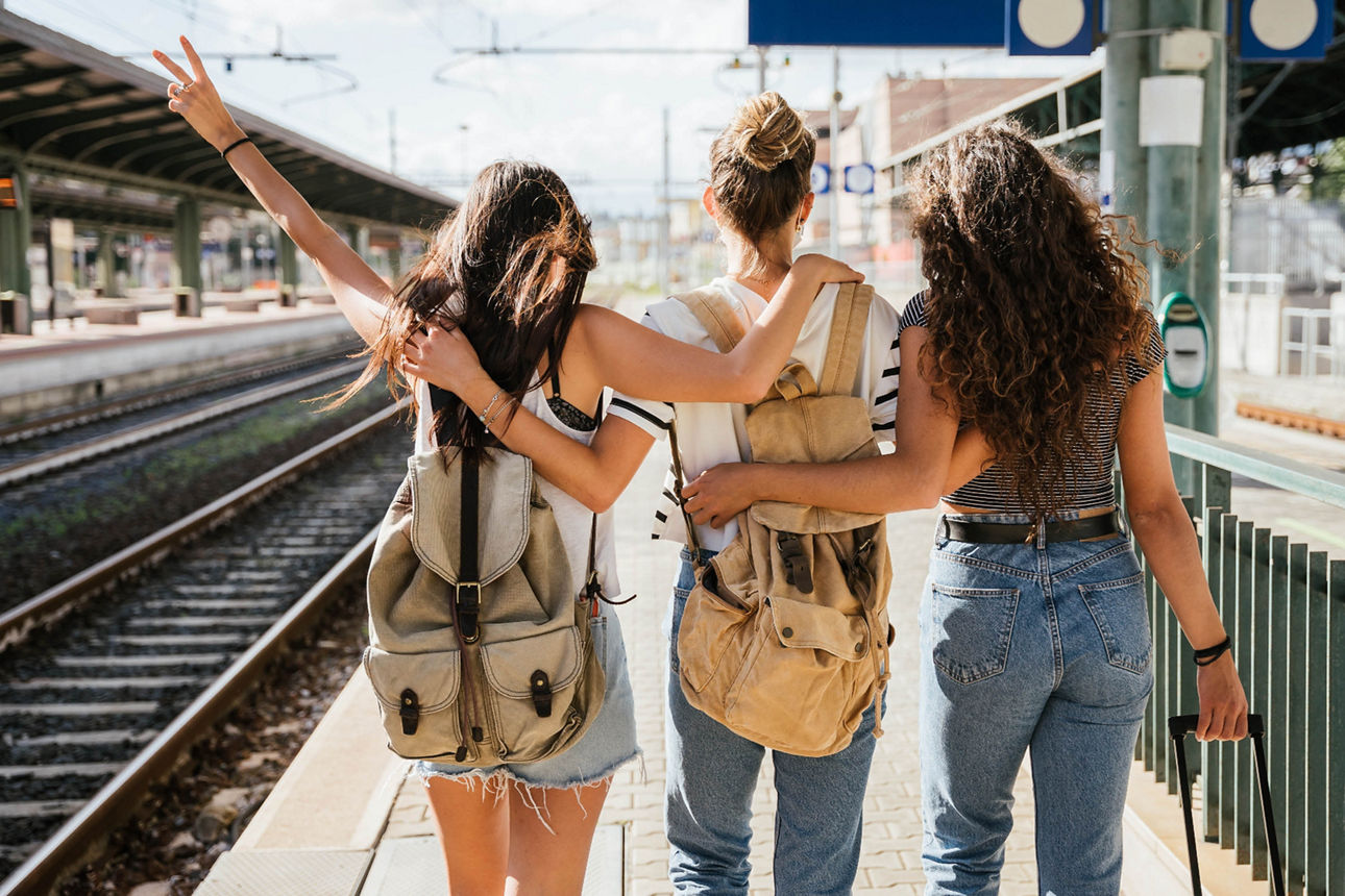 Bild von drei jungen Frauen mit Rucksäcken am Bahnhof