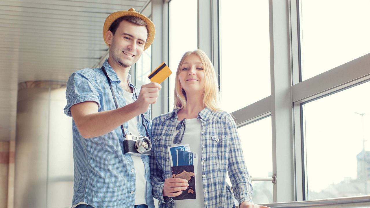 Bild von zwei Personen am Flughafen, die eine Kreditkarte und Reisepässe in den Händen halten.