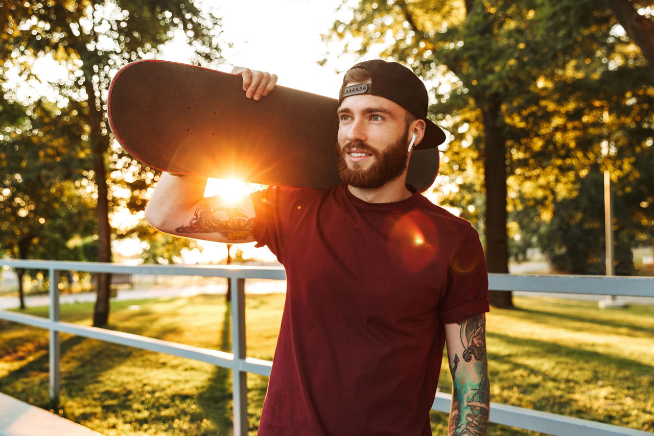 Junger Mann im Park trägt Scateboard auf seiner Schulter