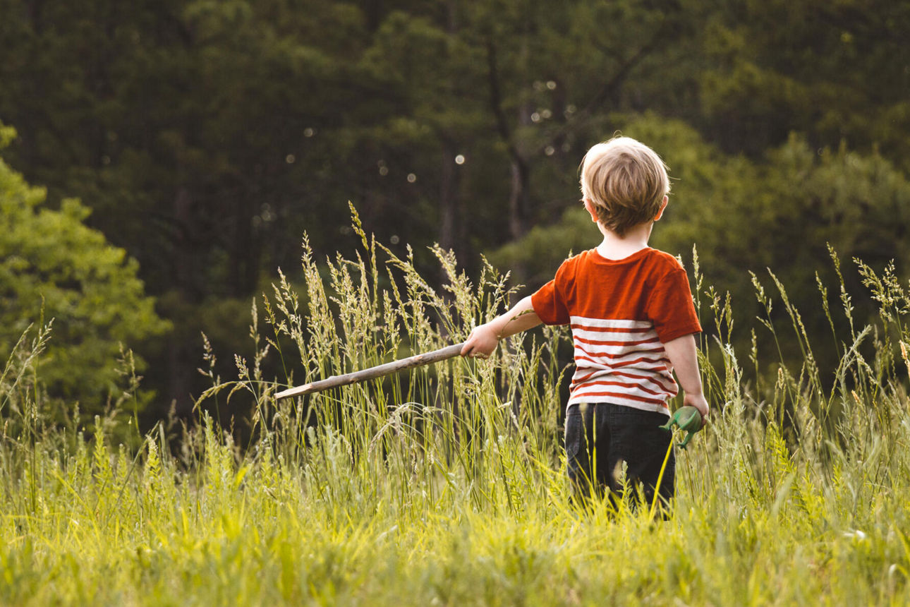 Ein kleiner Junge der auf einem Feld steht mit einem Stock.